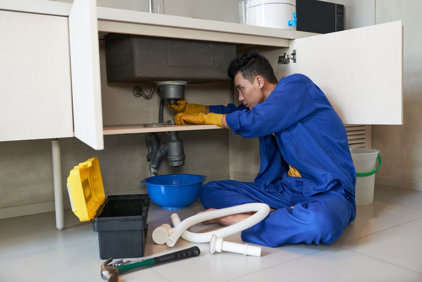 Plumber in blue overalls clearing a kitchen sink drain.